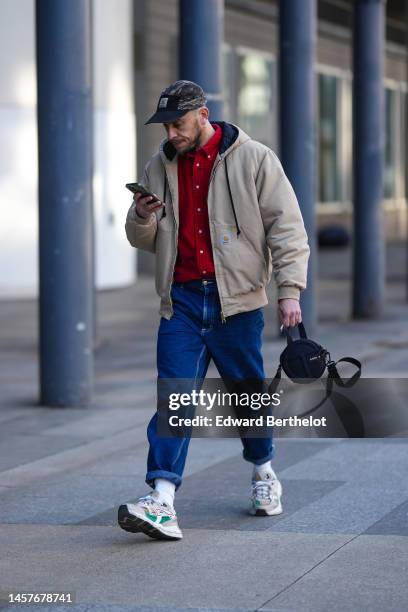 Guest wears a beige and khaki military print pattern cap from Carhartt, a red shirt, a beige hoodie zipper coat from Carhartt, blue denim large...