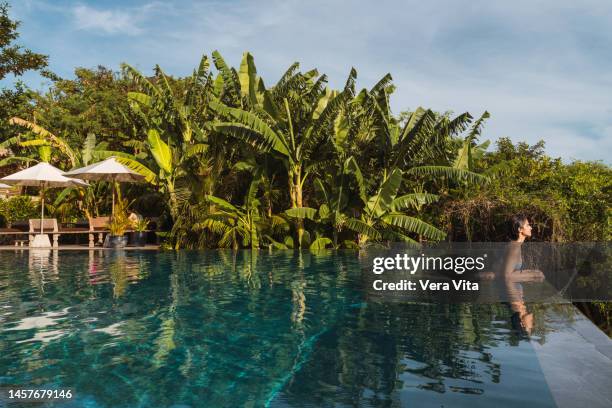 full length view of hispanic woman sunbathing swimming at tropical resort pool - bali spa stock pictures, royalty-free photos & images