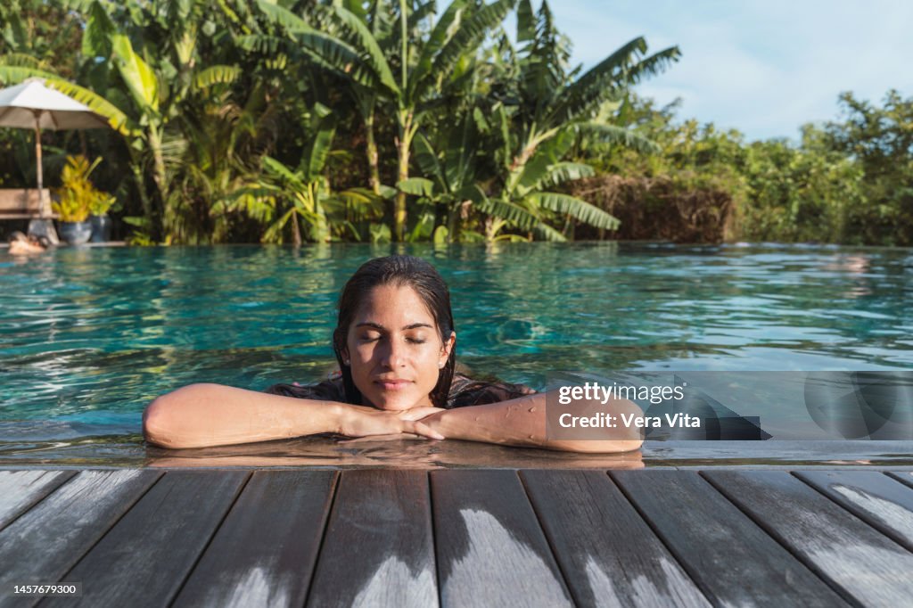Hispanic woman at hotel tropical resort sunbathing with palm trees in background