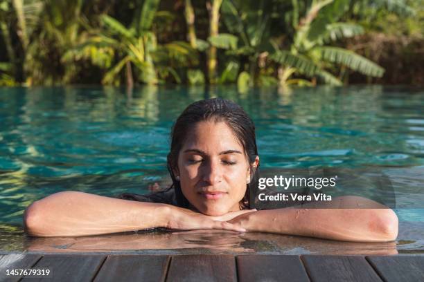 latin american woman relaxing swiming at hotel tropical resort with palm trees in background - bali spa stock pictures, royalty-free photos & images