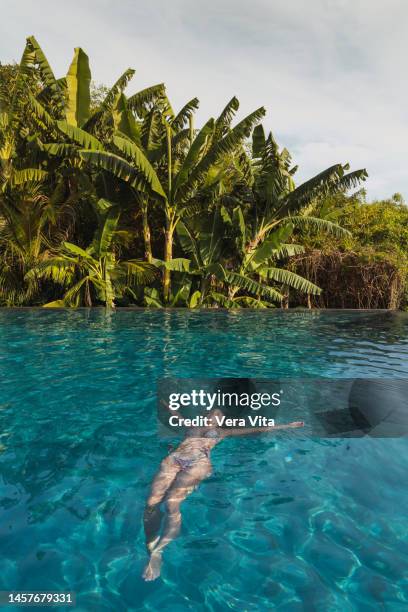 relax woman floating at tropical resort swiming pool with palm trees and turquoise water in background - schwimmer freisteller stock-fotos und bilder