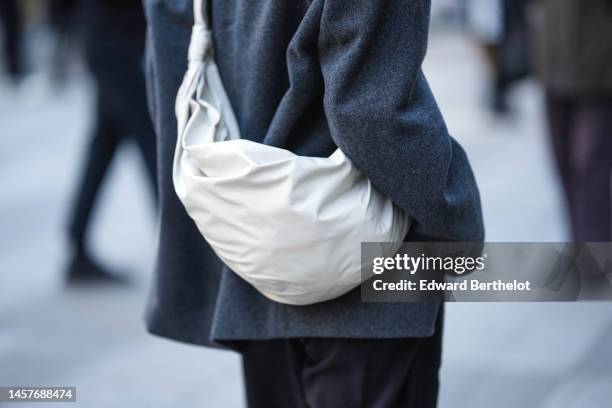 Guest wears a gray wool coat, black suit pants, a white shiny leather shoulder bag, outside Lemaire, during Paris Fashion Week - Menswear Fall-Winter...