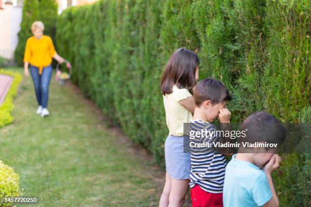mum hiding easter eggs while children cover their eyes - kid hide and seek stock pictures, royalty-free photos & images