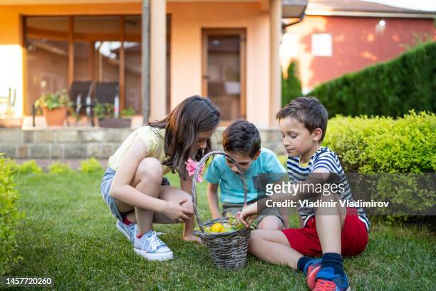 children sharing a basket of easter eggs in a garden - easter basket with candy stock pictures, royalty-free photos & images