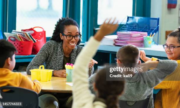 teacher in classroom points to student raising hand - criança de escola primária imagens e fotografias de stock