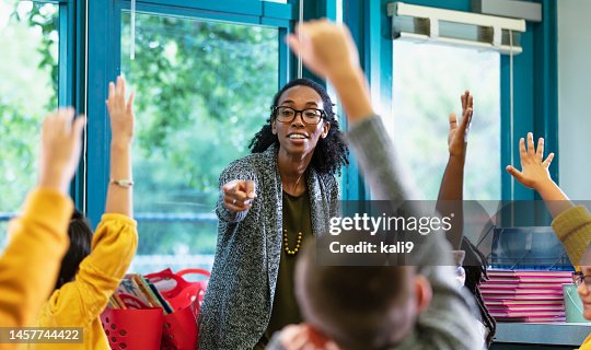 Teacher in classroom points to student raising hand