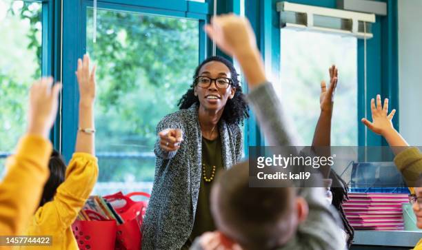 teacher in classroom points to student raising hand - elementary age 個照片及圖片檔