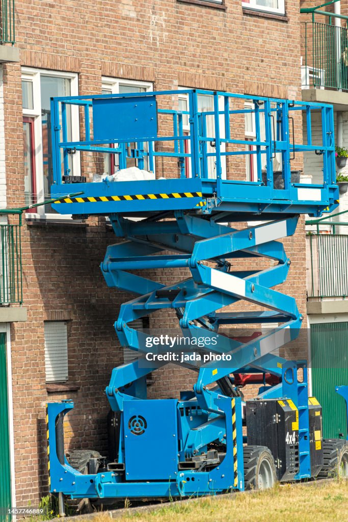 Blue scissor lift platform parked in front of an apartment building