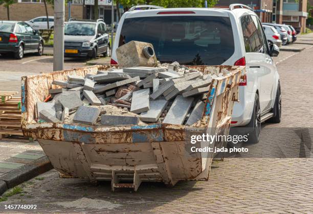 steel industrial open waste container filled with stone waste placed on the street behind a white car - detriti foto e immagini stock
