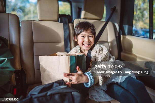 lovely cheerful girl sitting in car, smiling joyfully at the camera while holding a paper bag of takeaway food from drive through - drive through stock-fotos und bilder