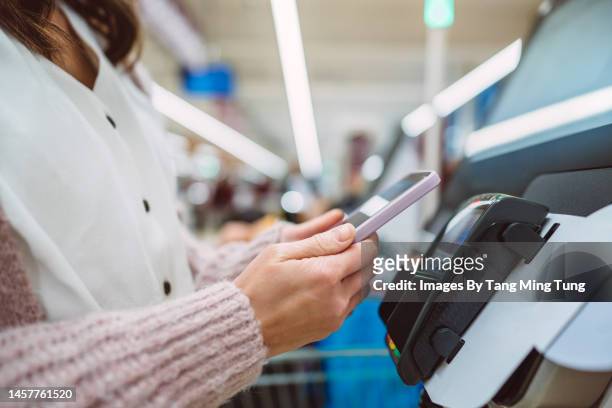a female shopper making contactless payment using smartphone at self-service checkout in supermarket - self service stock pictures, royalty-free photos & images