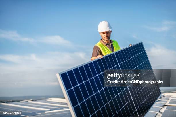 worker carrying solar panel on rooftop. - empreiteiro de reparações imagens e fotografias de stock