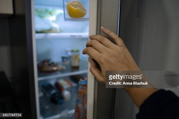 female hand close-up opening a fridge door with food at home - fridge door stock-fotos und bilder