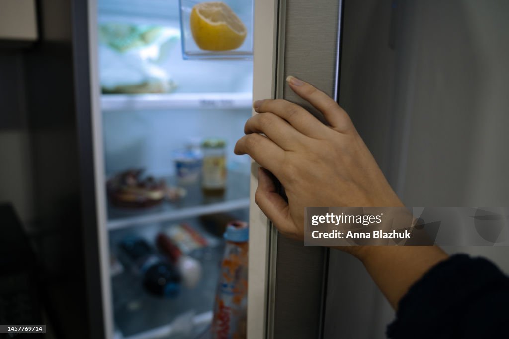 Female hand close-up opening a fridge door with food at home