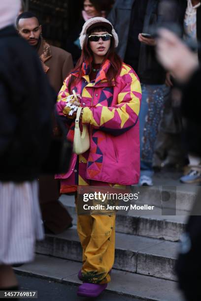 Fashion week guest seen wearing a pink and yellow patterned jacket and yellow pants with a Gucci cap and fluffy earmuffs, purple Crocs and sunglasses...