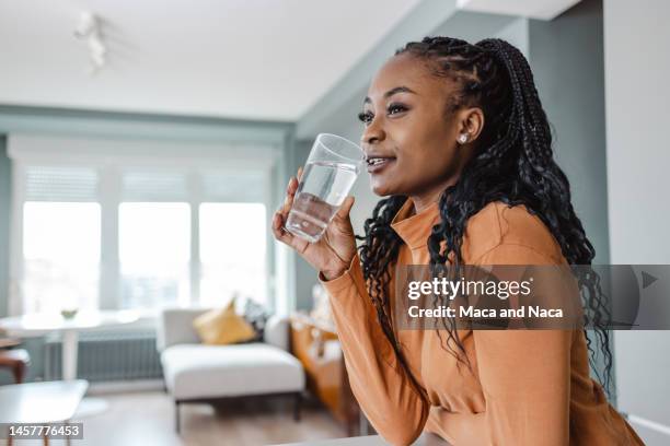mujer joven bebiendo agua en casa - agua potable fotografías e imágenes de stock