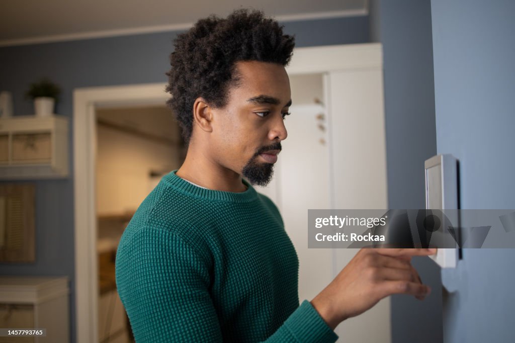 Junger Mann stellt die Temperatur zu Hause mit einem Gerät an der Wand ein