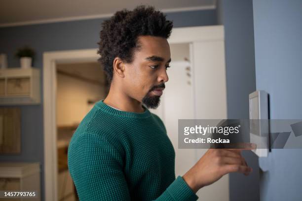 joven ajusta la temperatura en casa con un dispositivo en la pared - thermostat fotografías e imágenes de stock