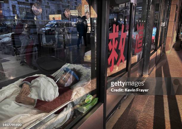 Patient wears a face shield as she lays on a gurney in the closed entrance way of an emergency room being used as an overflow area at a hospital on...