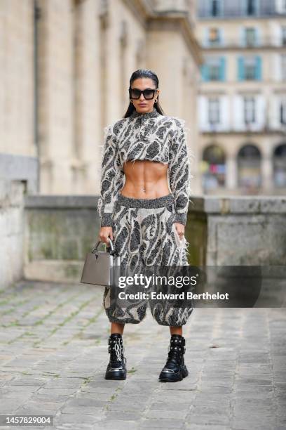 Jessica Aidi wears black sunglasses, gold earrings, a white latte and black wool ripped yoke high neck / long sleeves / cropped pullover from Louis...