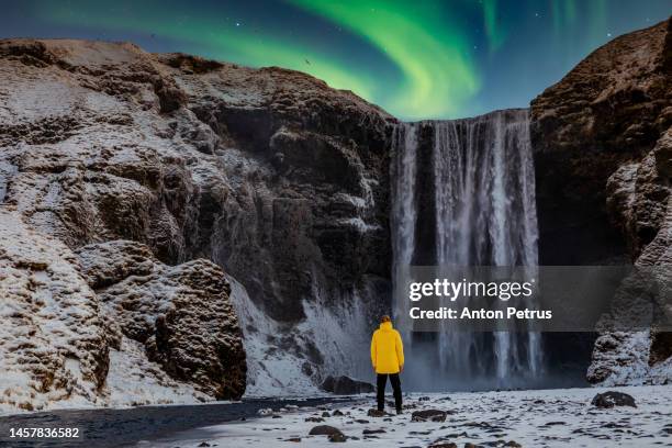 man on the background of skogafoss waterfall at night with northern lights - skogafoss waterfall stock pictures, royalty-free photos & images