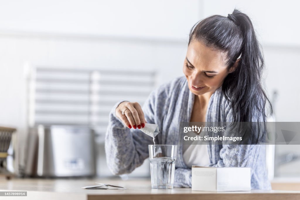 A young woman pours magnesium nutritional supplement into a glass of water.