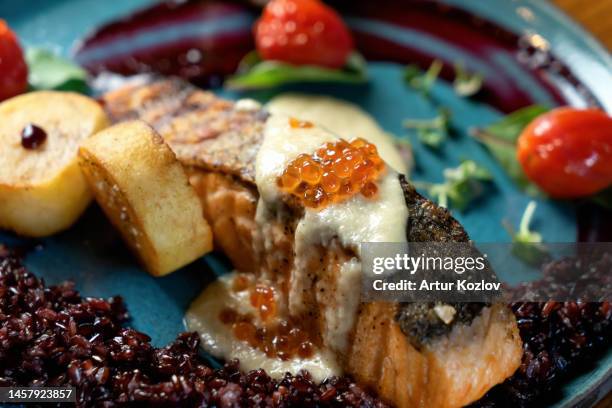 baked salmon with garnish on blue plate. garnish of vegetables, salmon served with sauce and caviar. soft focus. close-up - omega 3 fish stock pictures, royalty-free photos & images