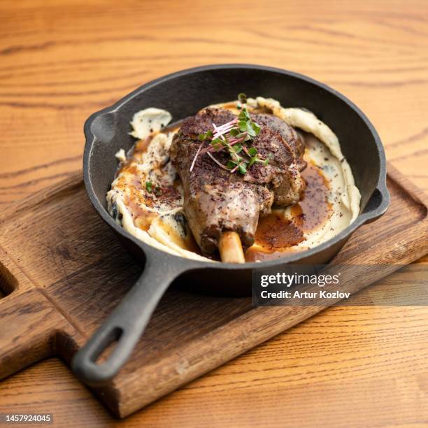 lamb with garnish and sauce in frying pan on wooden board. baked lamb garnished with microgreens. arabic cuisine.wooden background. soft focus. view from above - halal stock pictures, royalty-free photos & images