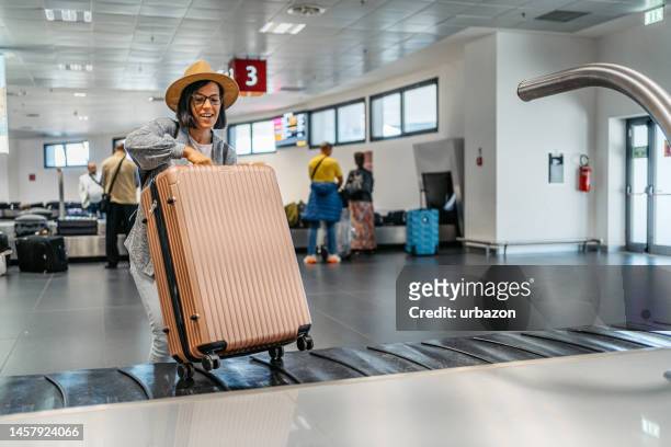 mujer joven recogiendo su equipaje del carrusel de equipaje en el aeropuerto - zona de equipajes fotografías e imágenes de stock