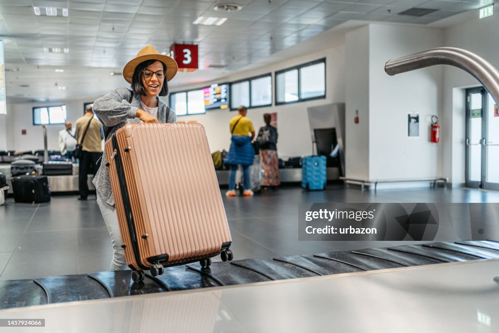 Young Woman Picking Up Her Luggage From The Baggage Carousel At The Airport