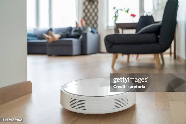 woman relaxing while robotic vacuum cleaner working - automated clearing house foto e immagini stock