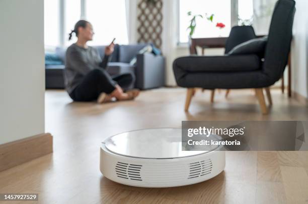 woman relaxing while robotic vacuum cleaner working - automated clearing house foto e immagini stock