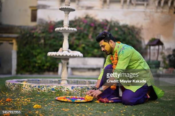 a man with a painted face and plate full of colours and flowers sitting in the courtyard of a palace in rajasthan - indian festivals stock-fotos und bilder