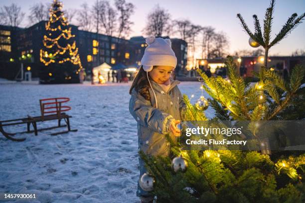 toddler girl, decorating the small christmas tree int he city during dusk - christmas atmosphere stock pictures, royalty-free photos & images