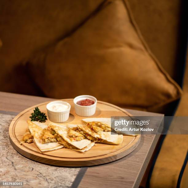 pita with stuffing and sauces on wooden board. asian cuisine. sliced pita bread with red and white sauce. dish on table against background of sofa. quick snack. soft focus, side view. copy space - lavash stockfoto's en -beelden