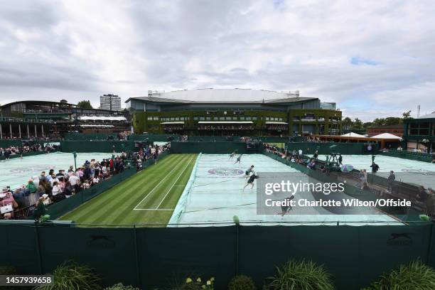 Grounds staff pull the waterproof covers off of the outside court with Centre Court looming in the distance during day one of The Championships...