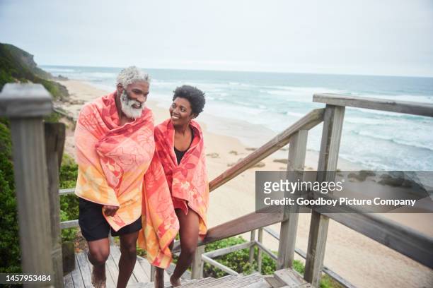 mature couple wrapped in towels walking up steps after an ocean swim - boardwalk stockfoto's en -beelden