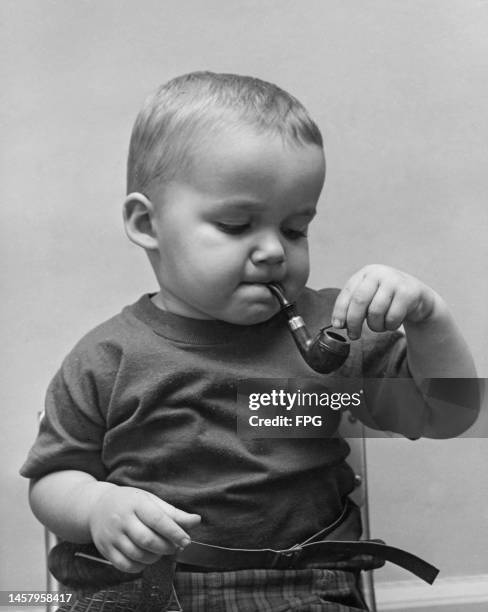 Young boy holding a pipe in his mouth as he holds an unlit match by the bowl of the pipe, United States, circa 1955.