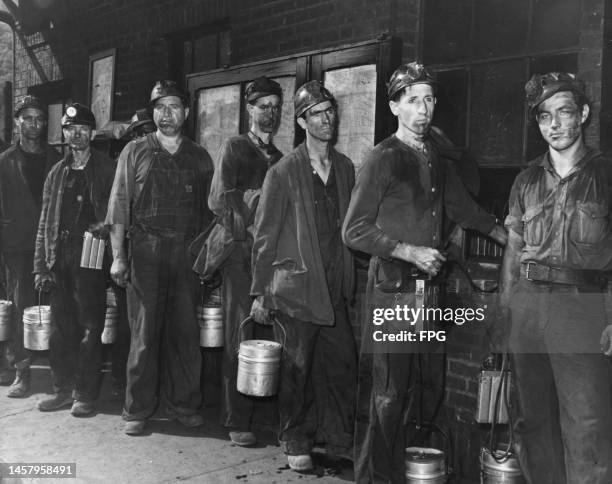 Coal miners, their faces smeared with coal dust, wearing helmets, all with lunch pales, with three carrying air quality detectors, as they queue for...