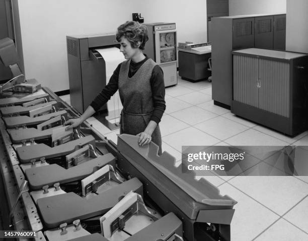 Female worker loading punch cards, the like of which are used to directly control automated machinery or in data processing applications, into an...