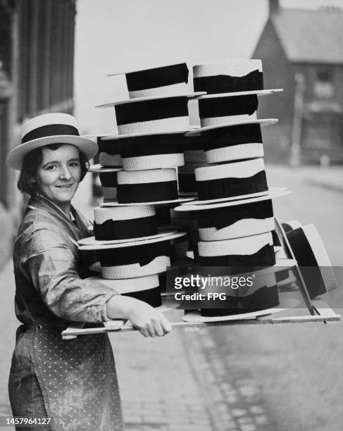 Woman carrying a consignment of straw boater hats outside an factory in St Albans, Hertfordshire, England, 7th March 1936.