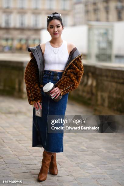 Guest wears black sunglasses, a white tank-top / cropped tank-top from Louis Vuitton, a brown LV monogram print pattern fluffy bomber coat from Louis...