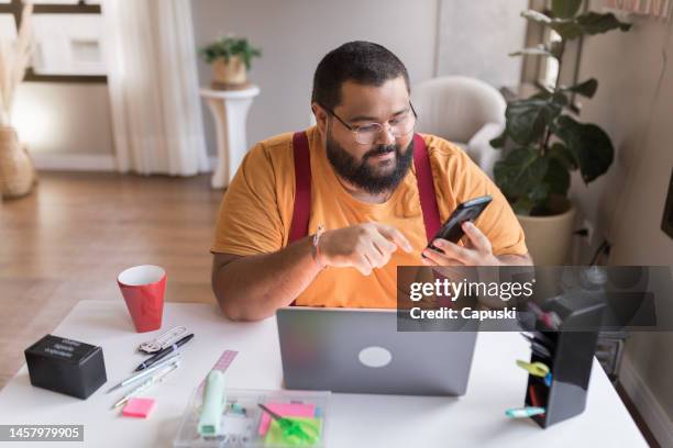 mann, der sein telefon überprüft, während er von zu hause aus arbeitet - kräftig gebaut stock-fotos und bilder