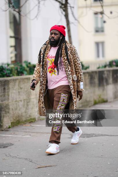 Guest wears a red cut-out wool ribbed beanie, a pale pink with red and yellow print pattern t-shirt, a beige and brown leopard print pattern fluffy...