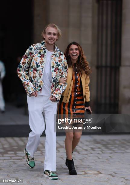 Lucas Portman and Zoe Coleman seen wearing a full Louis Vuitton Look, white pants, colorful Shirt and beige jacket and orange and black leather dress...