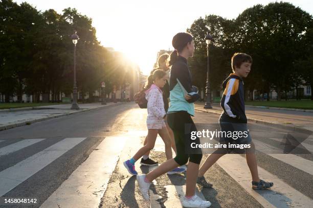 group of people made up of children and adults crossing the street on the crosswalk, in the background there are trees and public lighting. - centre ville france photos et images de collection