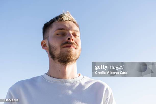 a smiling man in his twenties breathing fresh air at sunset - einatmen stock-fotos und bilder