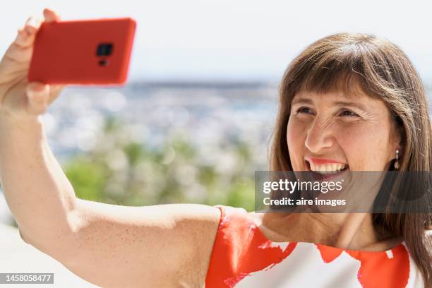 woman standing in the open air with a big smile while holding her phone and taking a selfie - open hair selfie stock pictures, royalty-free photos & images