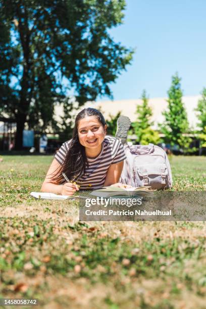 smiling student girl lying on the grass, taking notas by hand on a journal, on a sunny day after class. - world book day stock pictures, royalty-free photos & images