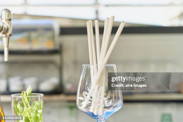 glass wine glass containing a group of white straws together with a transparent vase and a water faucet. - disposable stock pictures, royalty-free photos & images